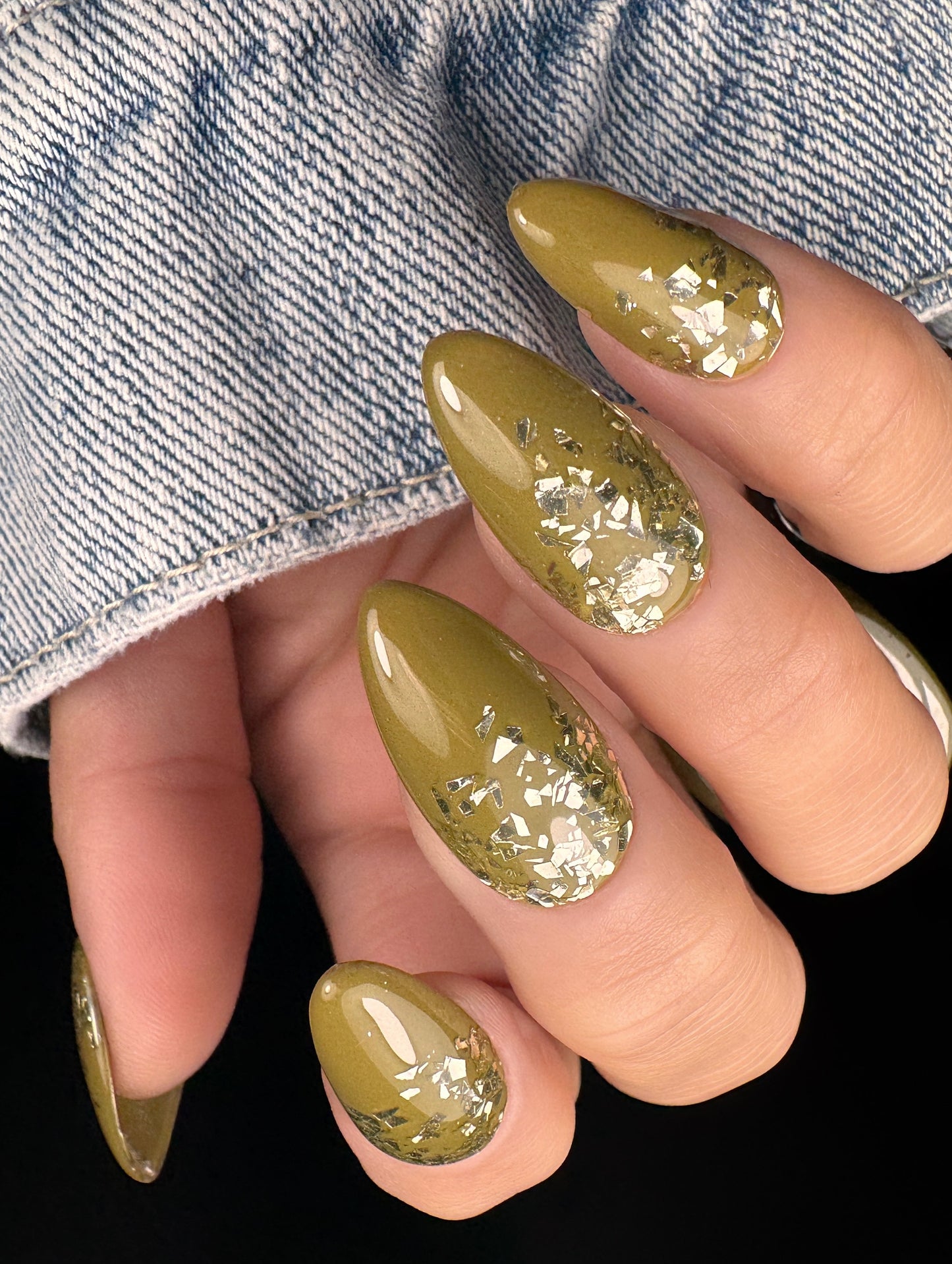 Hand with olive green gel color and glittery gold accents against a denim background