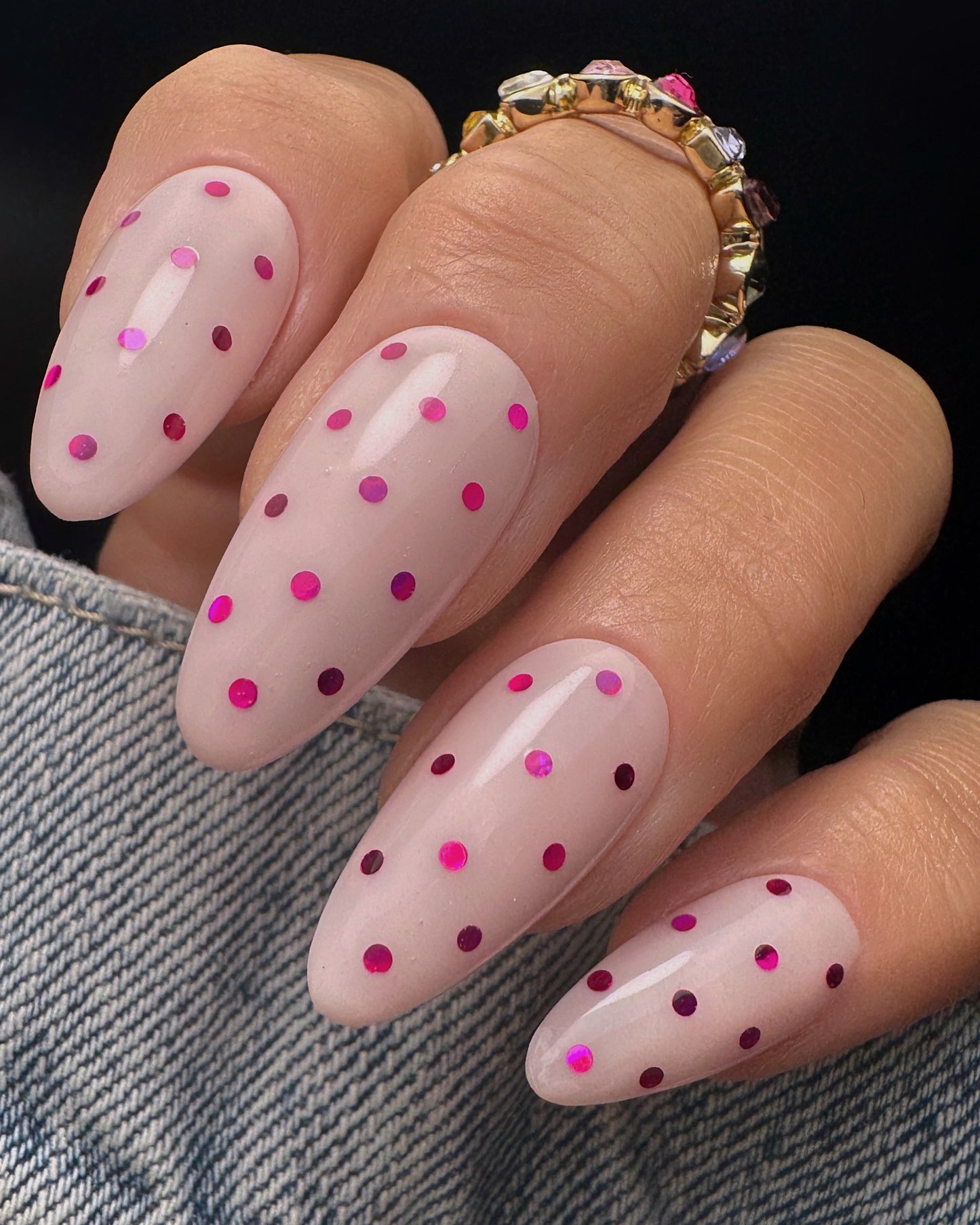 Nails with pink metallic polka dot design on a dark background