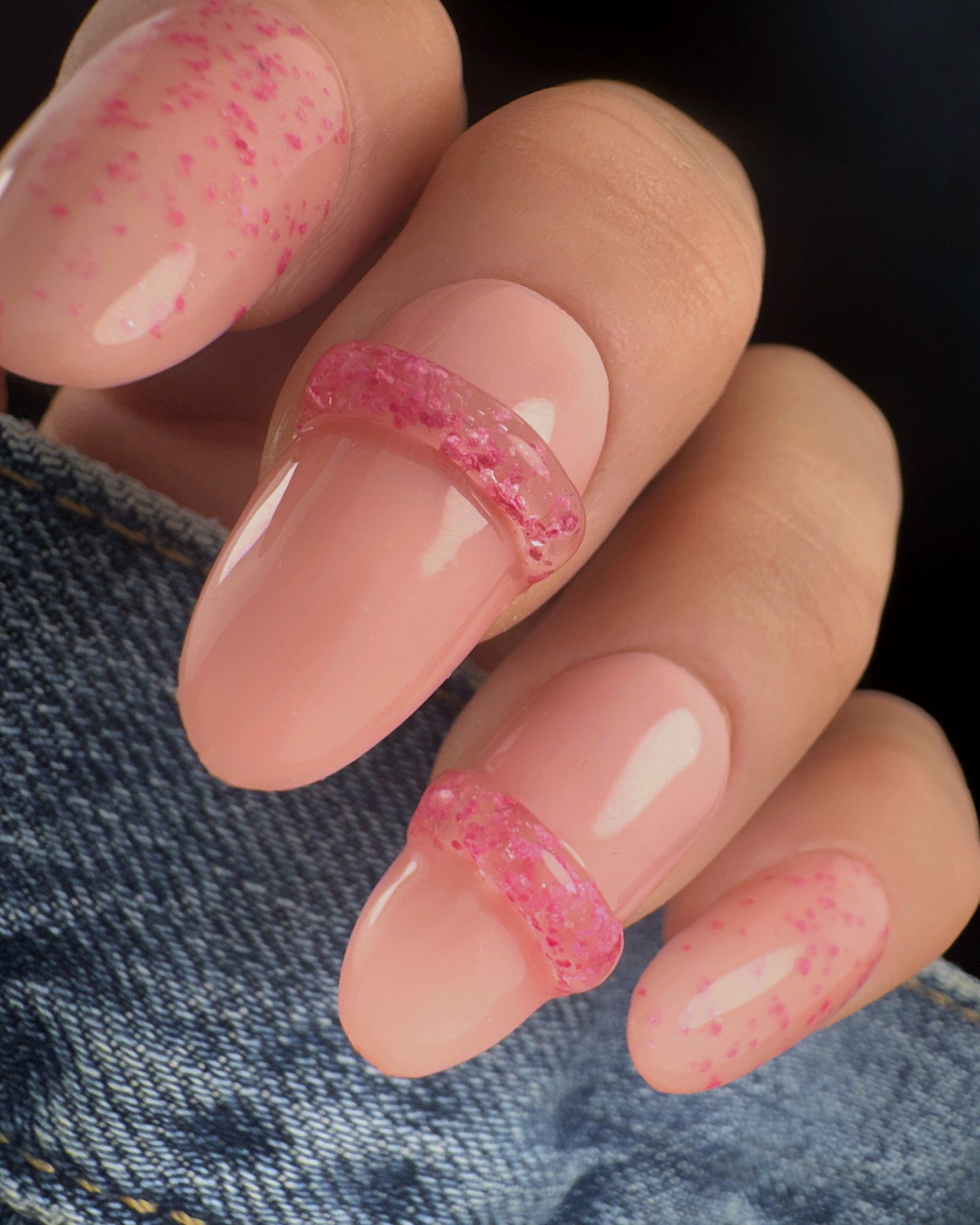 Close-up of nails with pink speckled design with clear 3D elements on a denim background