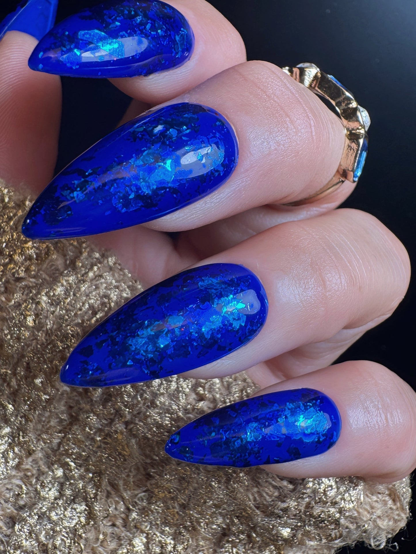 Close-up of a hand with blue glittery nail design on a gold and black background