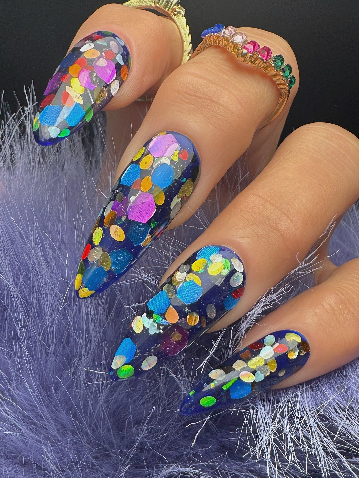 Nails with multicolored glitter design on a textured purple surface