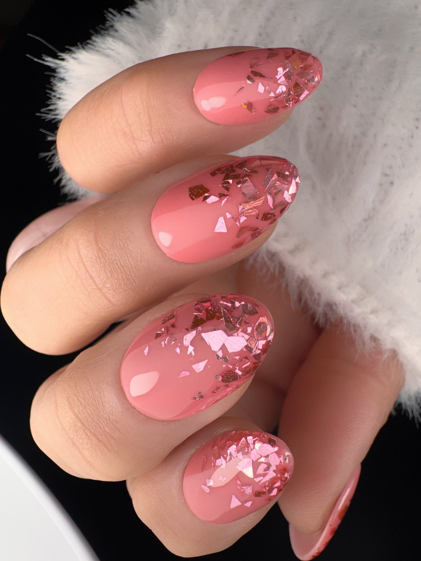 Close-up of a hand with pink glittery nail art on a white background