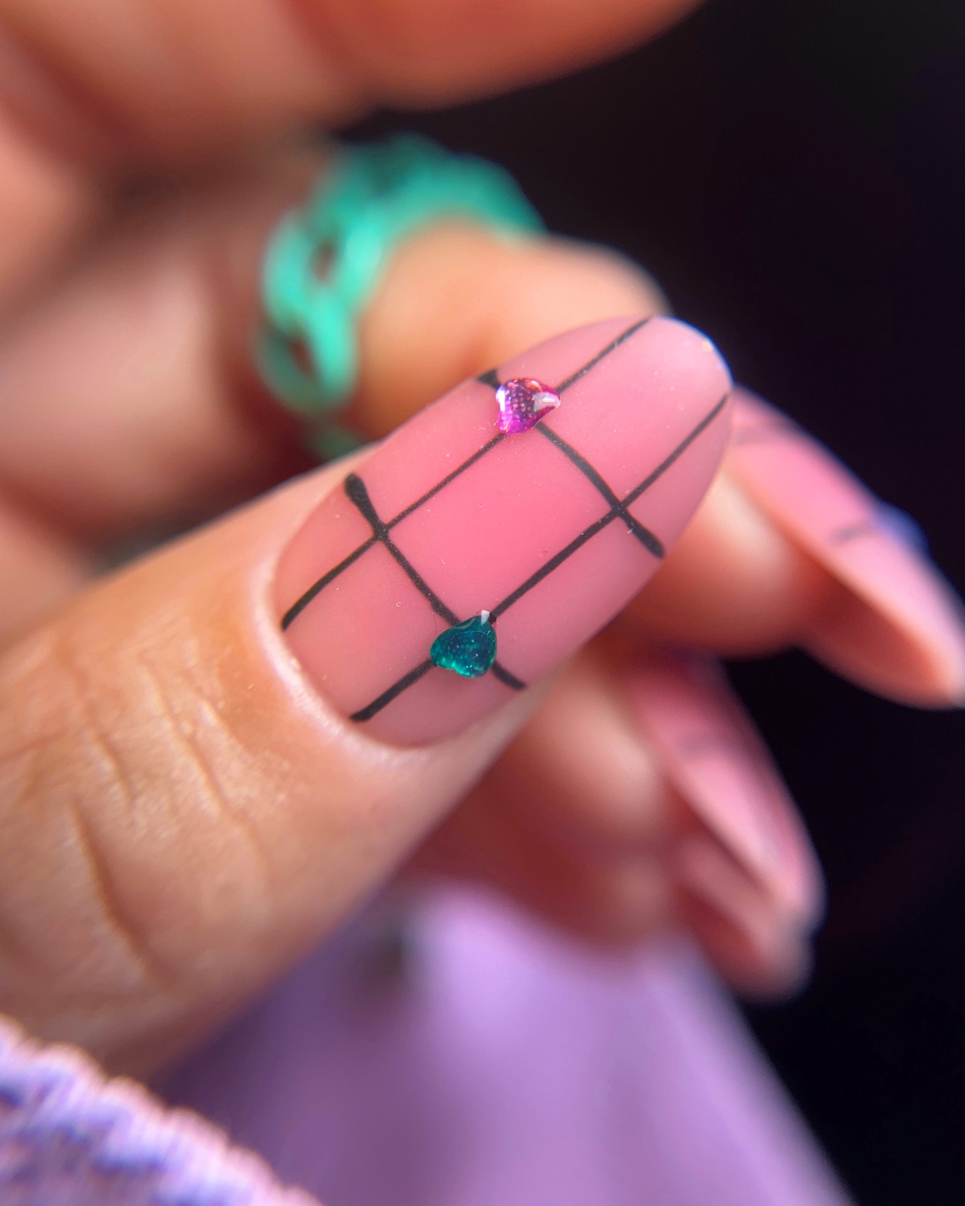 Nail art with grid pattern and colored hearts on a blurred background
