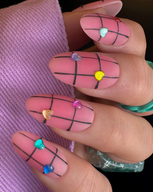 Nails with pink and black grid design, colorful hearts on a pink fabric background