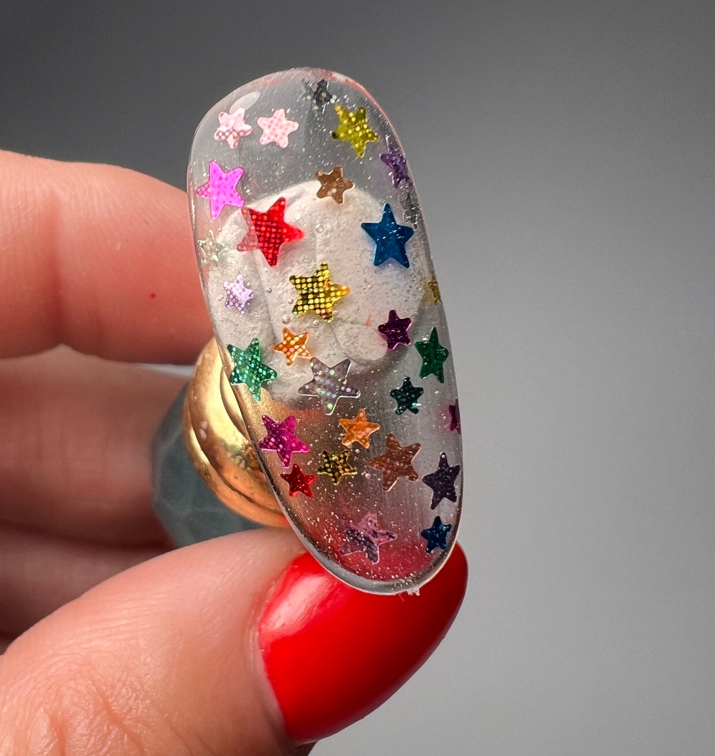 Hand holding nail art tip decorated with mullticolor star glitter on gray background.
