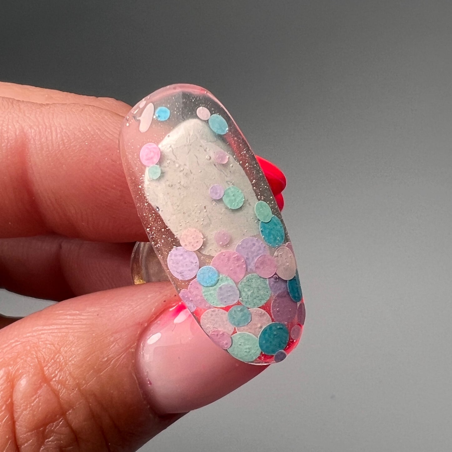Hand holding nail tip decorated wiuth pastel circle glitter on gray background. 