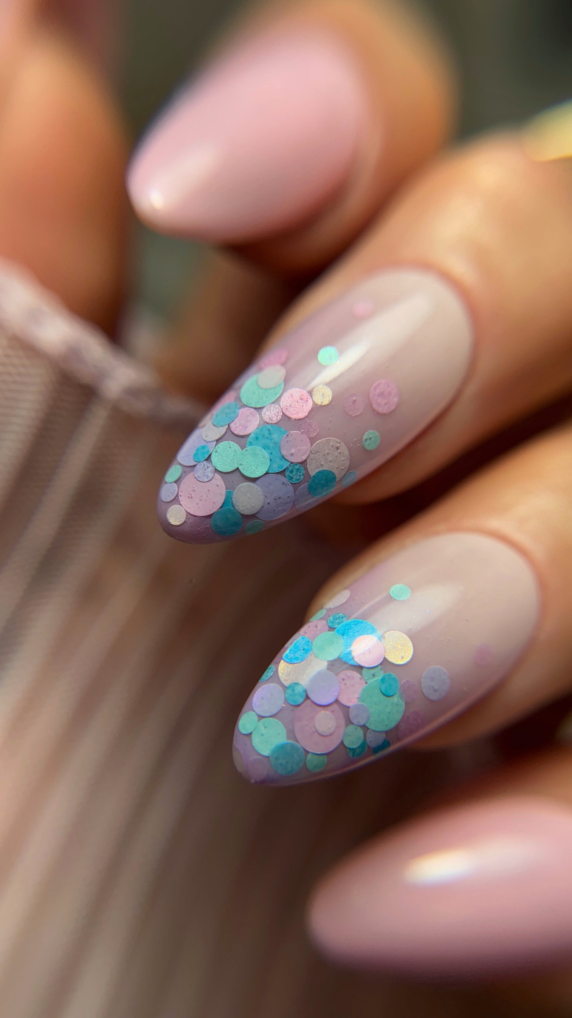 Nails with pastel color and confetti design held by a hand.