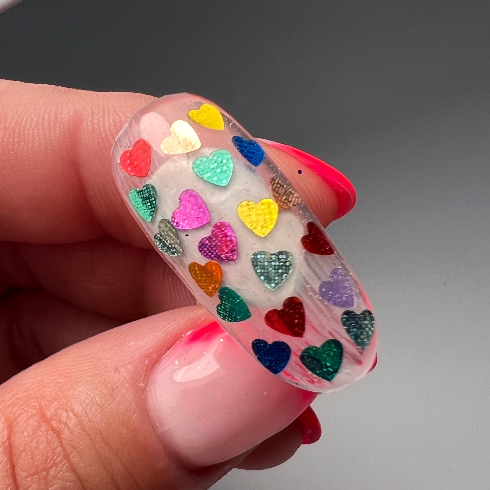 Hand holding tip with mulitolor heart glitter on gray background. 