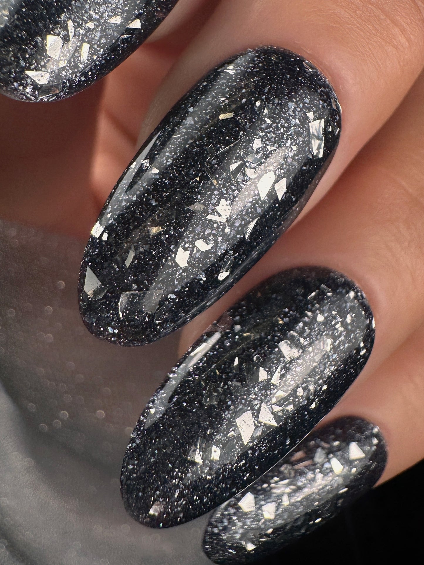 Close-up of black glittery nails on a neutral background
