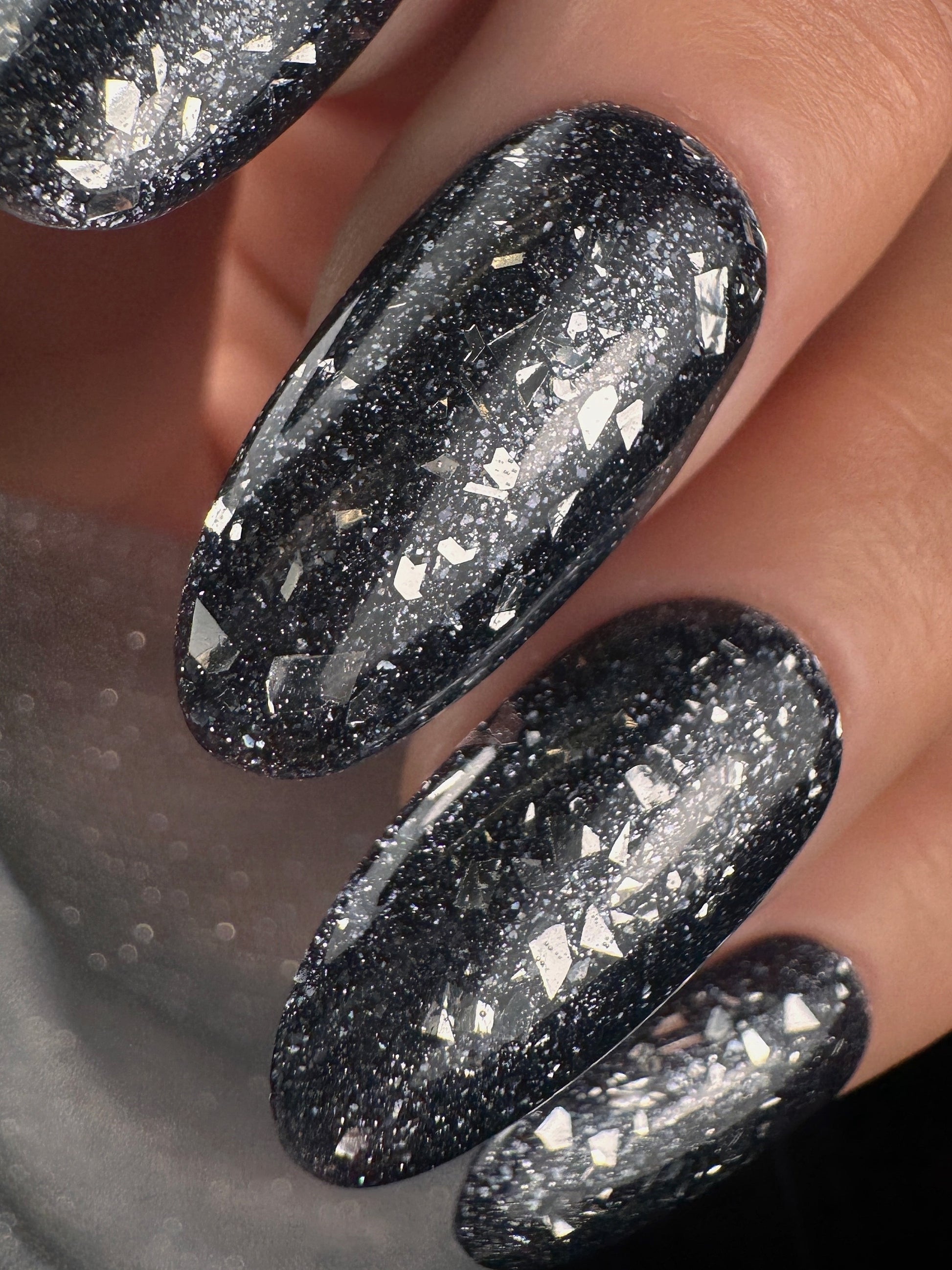 Close-up of black glittery nails on a neutral background