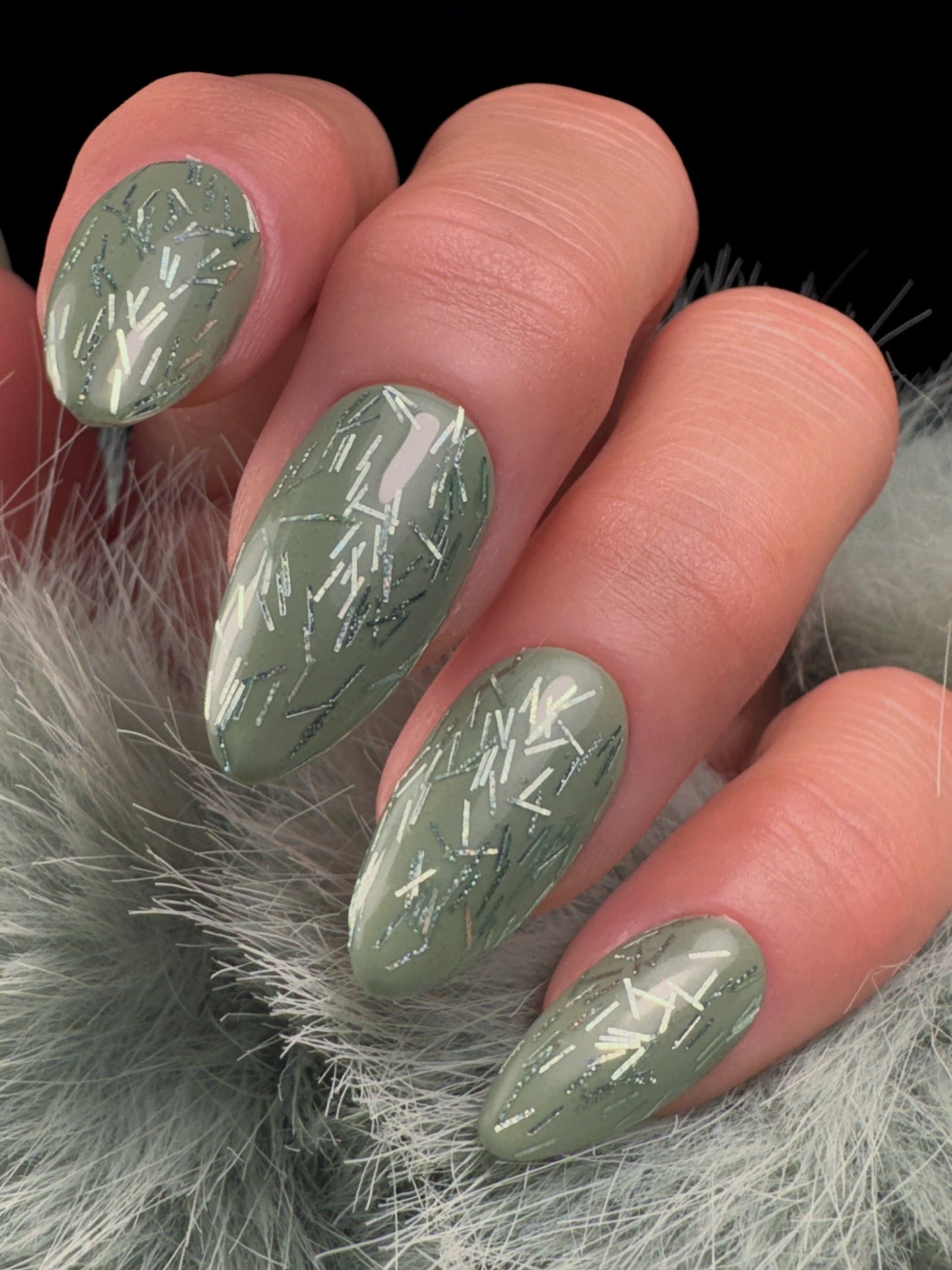 Nails with green glitter design and decorative elements on a green furry background