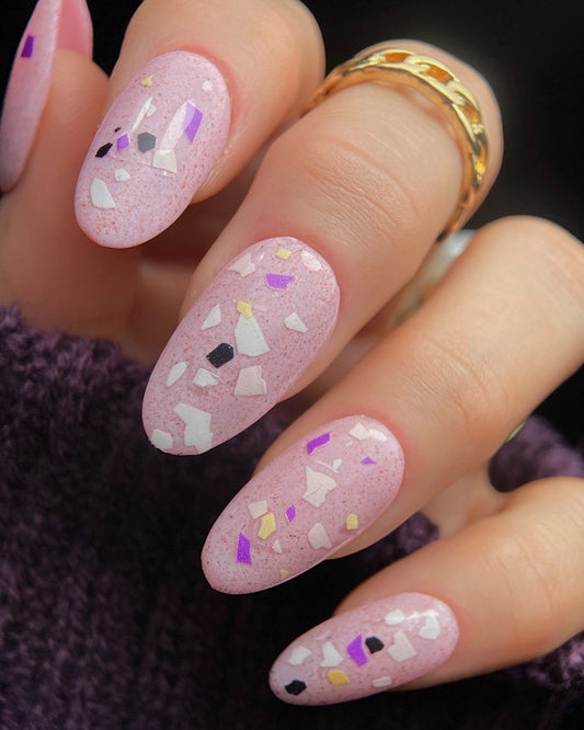 Close-up of manicured hand with pink terrazzo nail art.