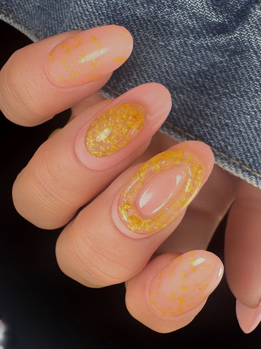 Close-up of nails with yellow speckled design with clear 3D elements on a denim background