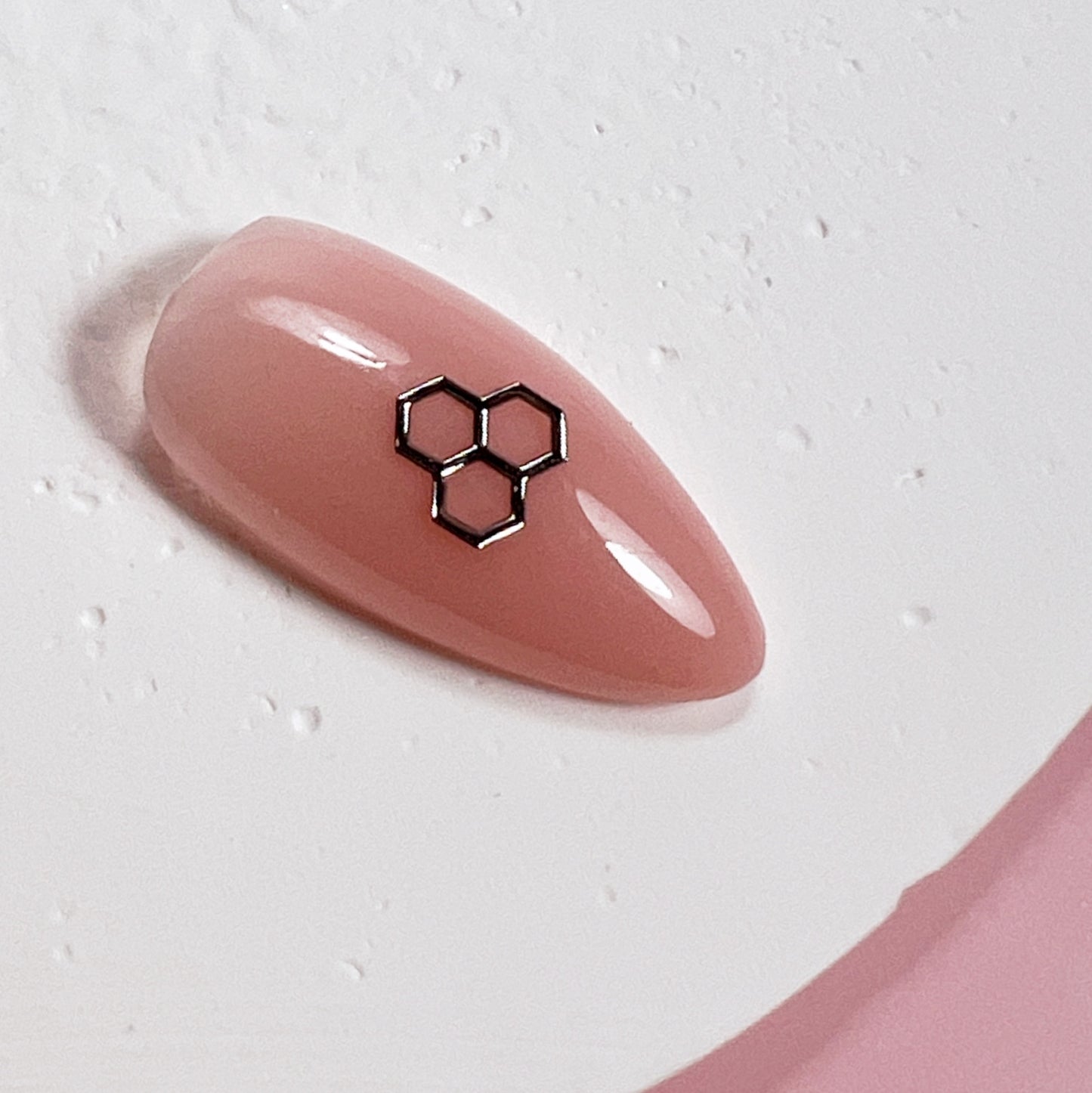 Come up of nail tip with silver honeycomb charm on white textured surface.