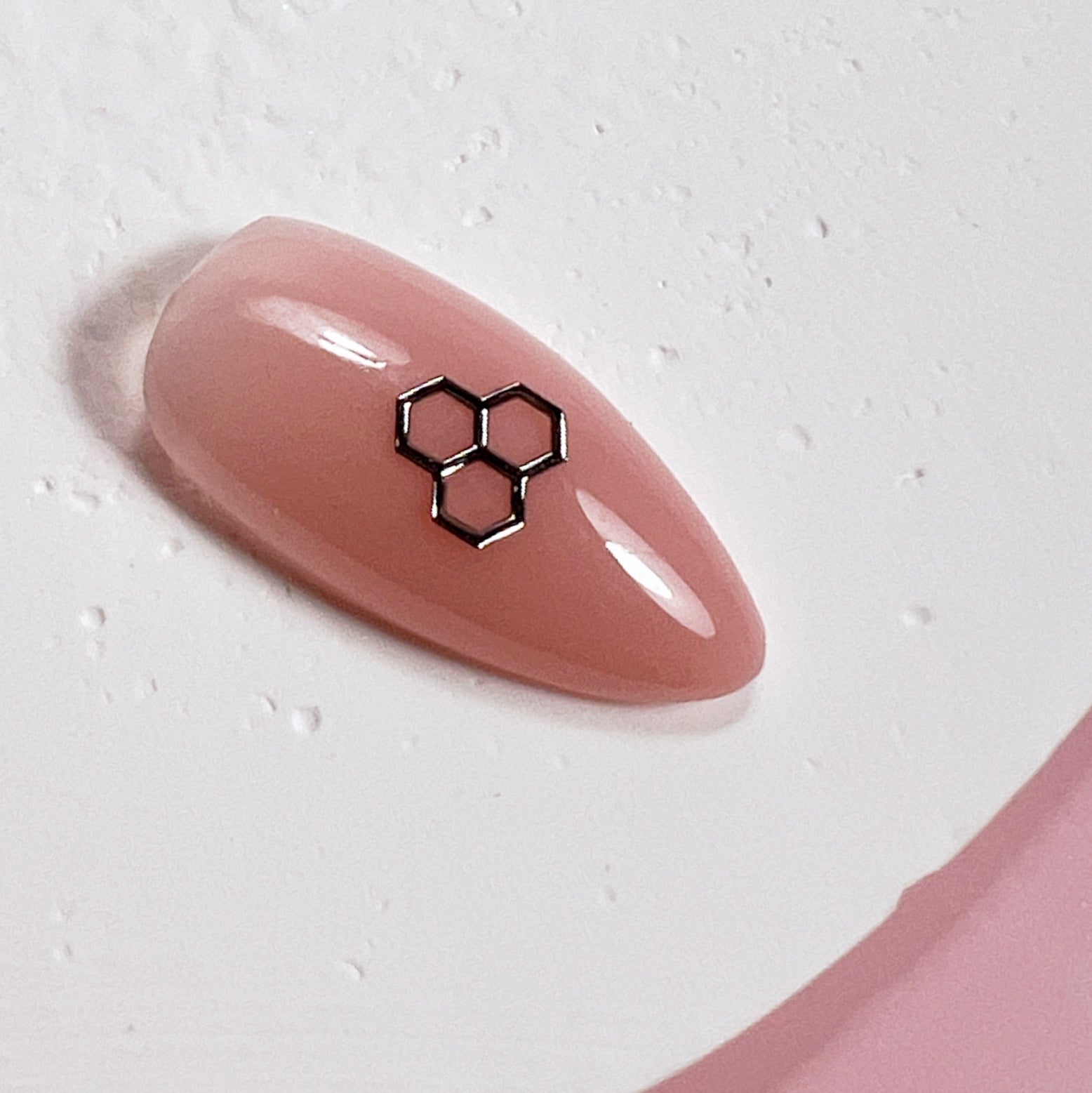 Come up of nail tip with silver honeycomb charm on white textured surface.