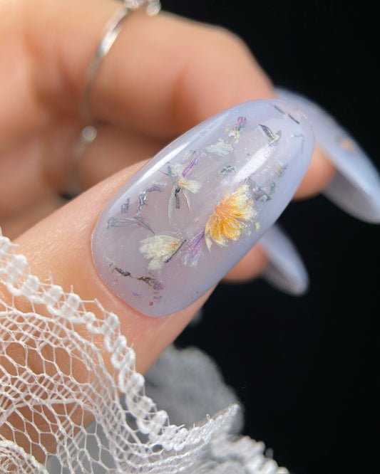 Nail with floral design held by a hand wearing lace gloves on a black background