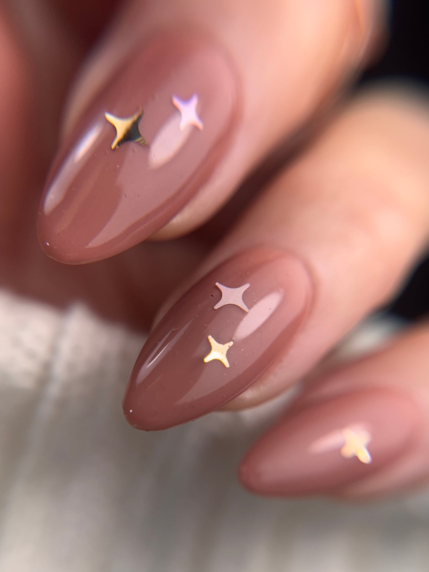 Nails with a nude color and star-shaped decorations on a neutral background