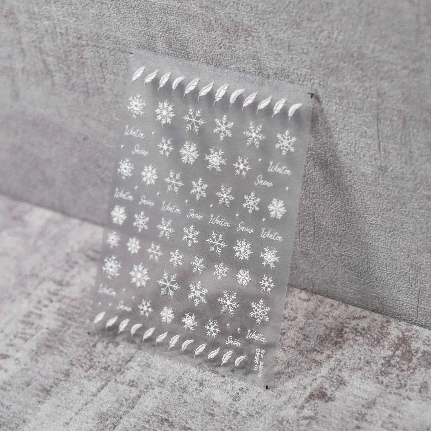Feathers & Flakes Nail Stickers - Raised Texture White Snowflake and Feather Nail Stickers on Clear Sheet, Gray Textured Background