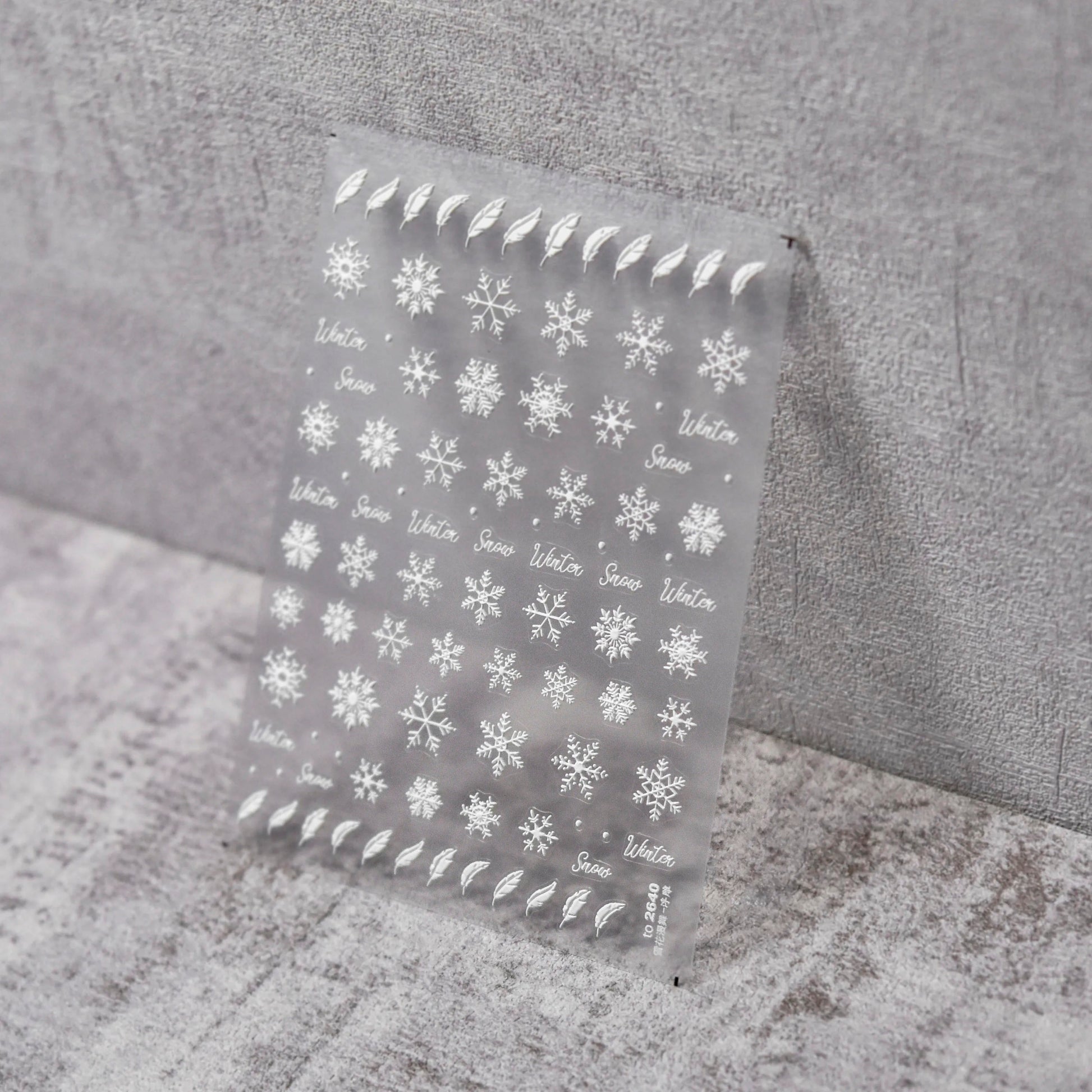 Feathers & Flakes Nail Stickers - Raised Texture White Snowflake and Feather Nail Stickers on Clear Sheet, Gray Textured Background