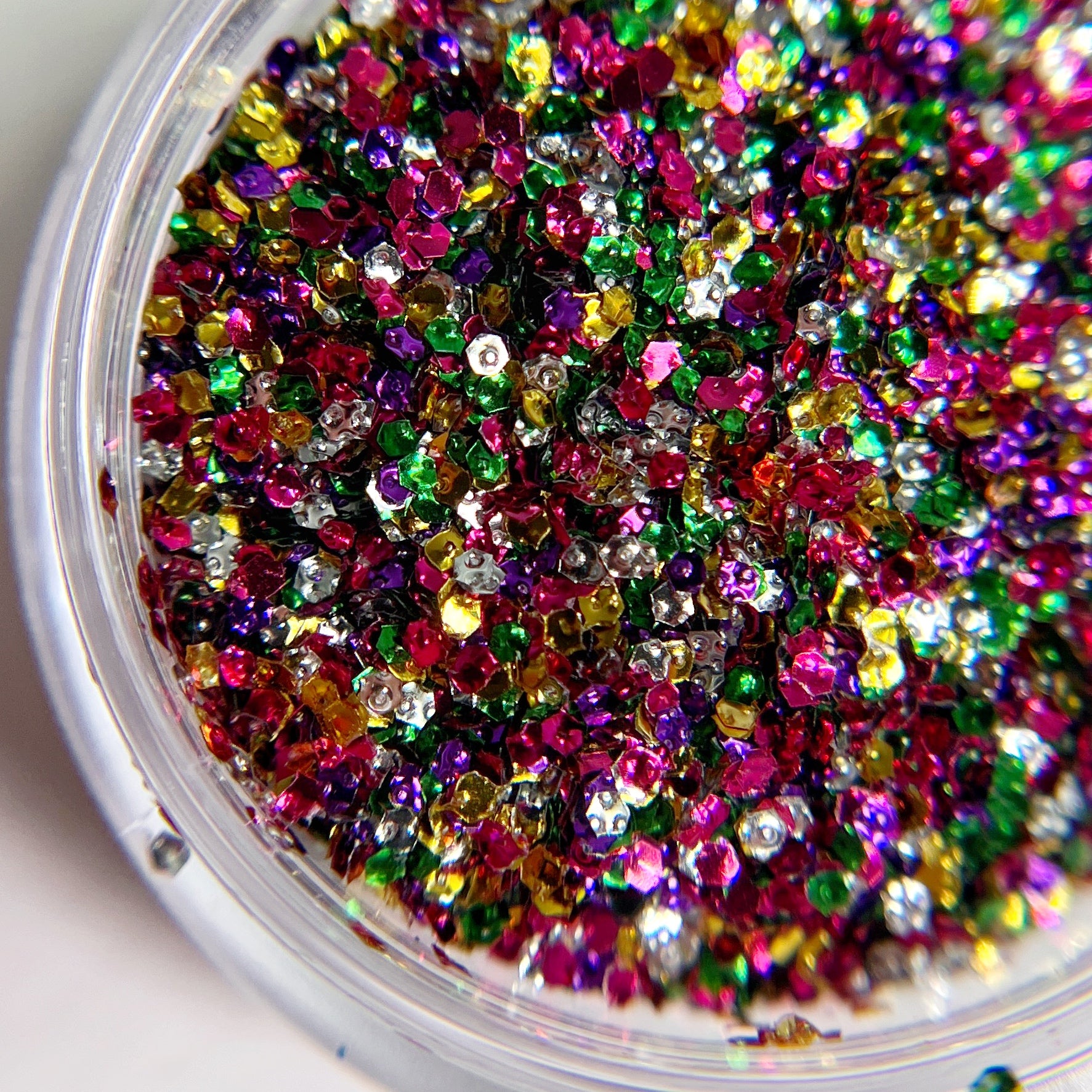 Detail view of multicolor round glitter in clear jar on white background. 