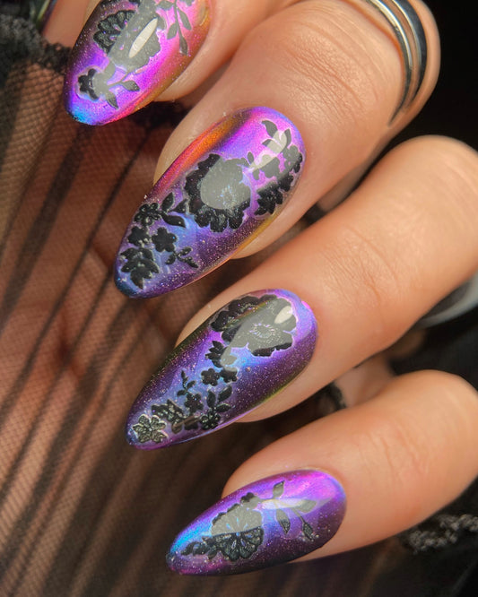 Nails with purple and black floral design on a hand wearing sheer black glove