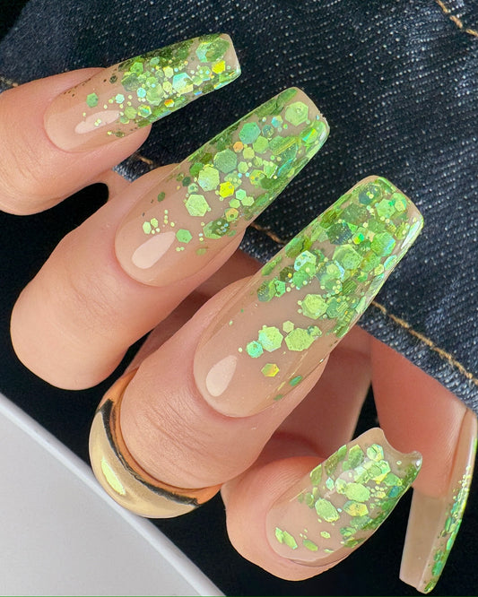 Green glittery nails with a clear base on a dark denim background
