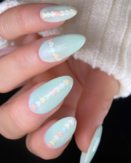 Mint green nails with heart-shaped decorations on a blurred background