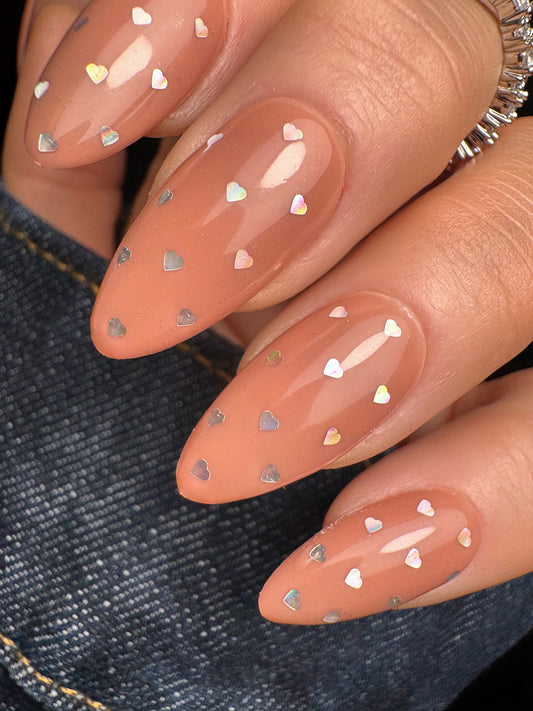 Nails with peach polish and heart-shaped decorations on a denim background