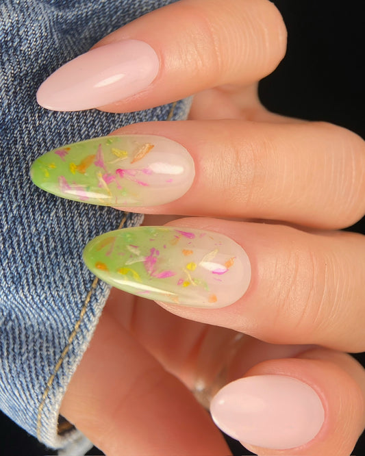 Close-up of a hand with green and pink floral nail art on a denim background