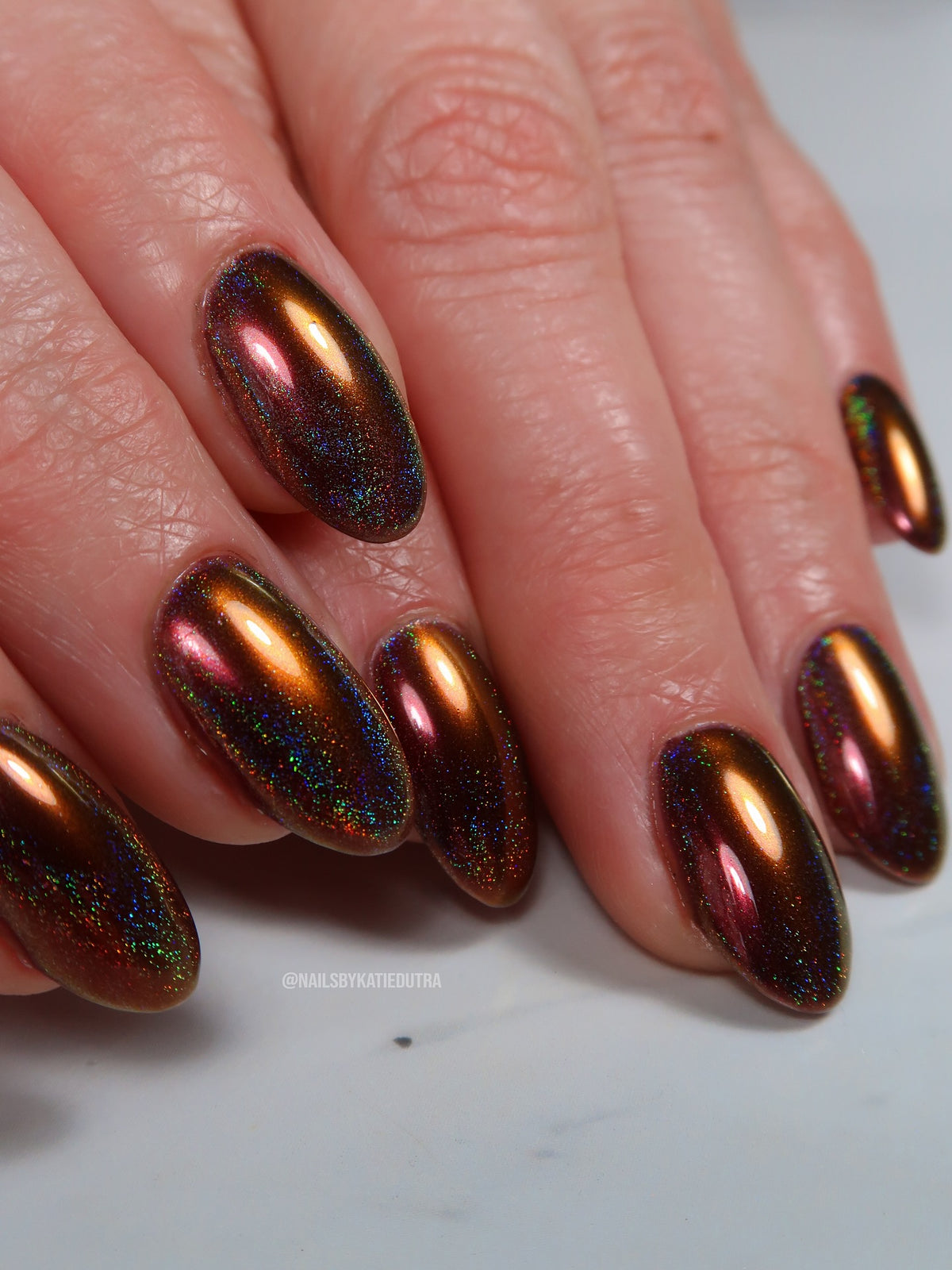Rich bronze multichrome manicure by Katie Dutra using Vacation Nail Shop Last Call Chrome, with copper, pink and gold shifts over a fine holographic sparkle base.