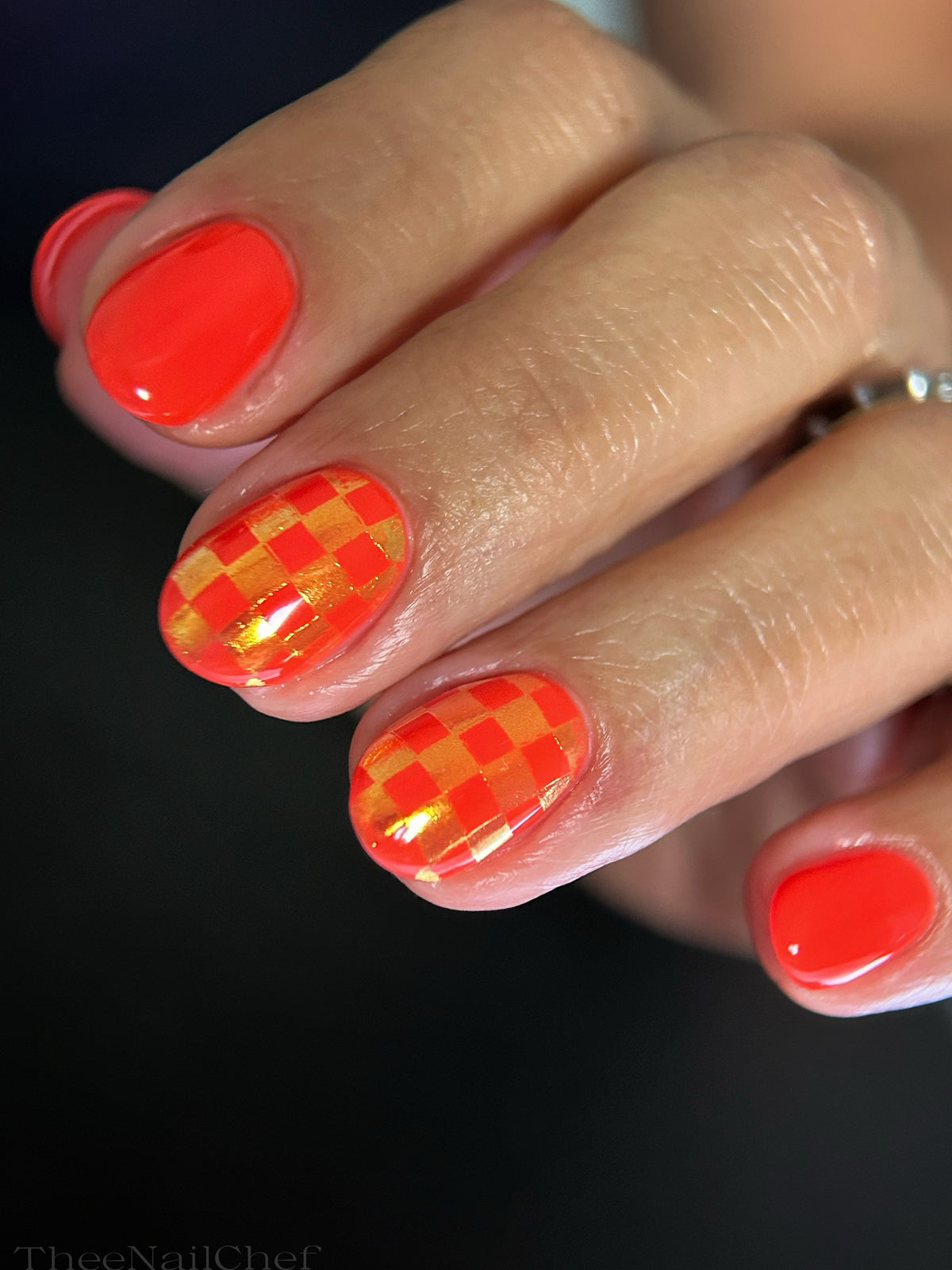 Bright orange manicure by Jennie Guthrie featuring a gold iridescent checkerboard design created with the Vacation Nail Shop Lucent Metal Chrome Palette.