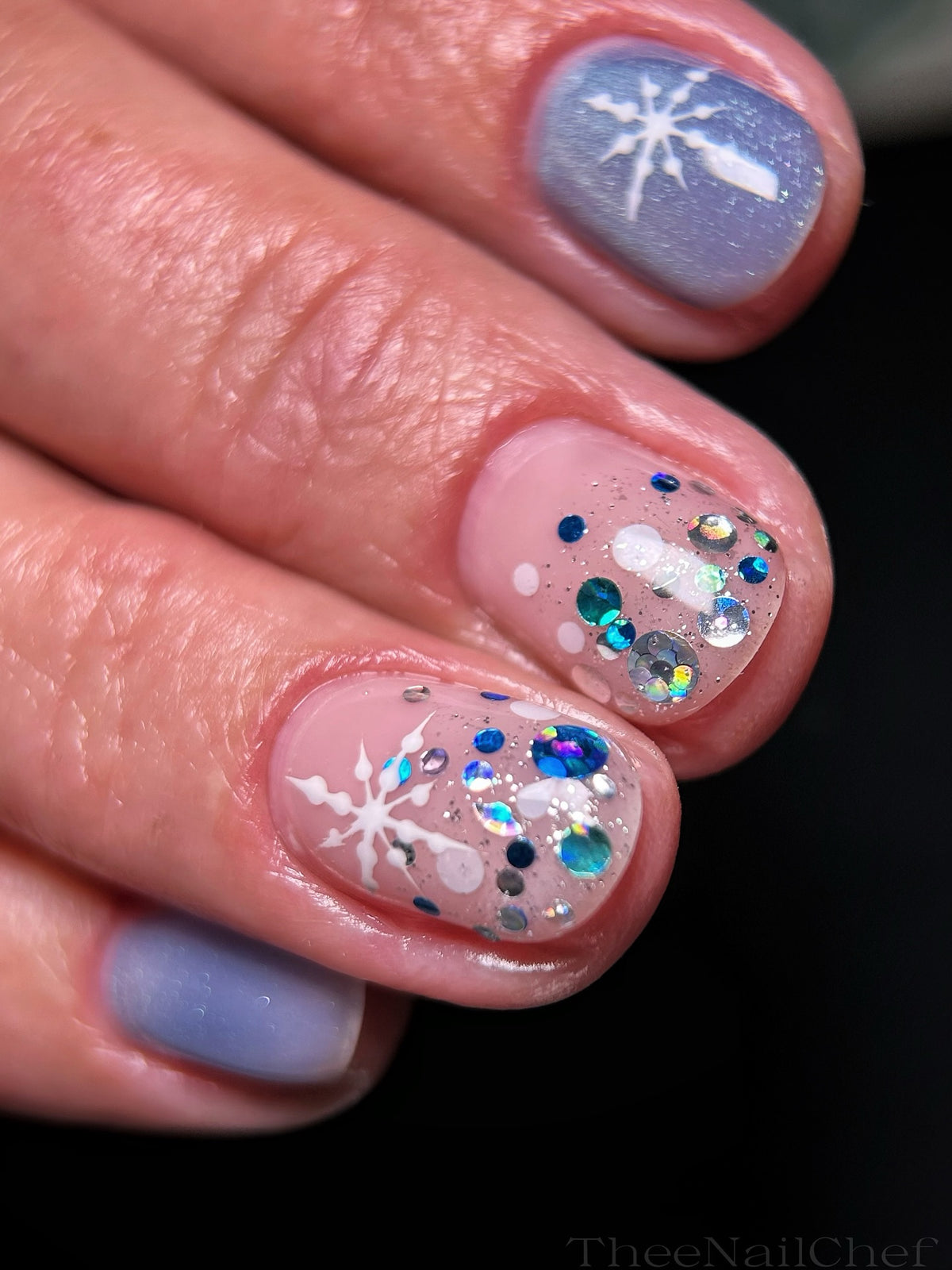 Winter nail art by Jennie Guthrie featuring Vacation Nail Shop Winter Blues Spots Glitter, with blue and iridescent glitter dots, silver sparkle and hand-painted white snowflakes.