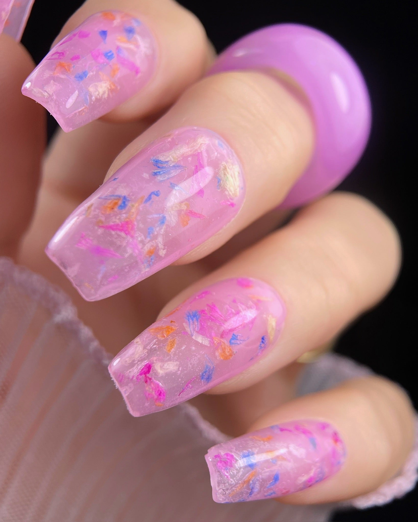 Close-up of a hand with pink gel nails featuring colorful flowers on a dark background