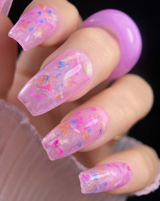 Close-up of a hand with pink gel nails featuring colorful flowers on a dark background