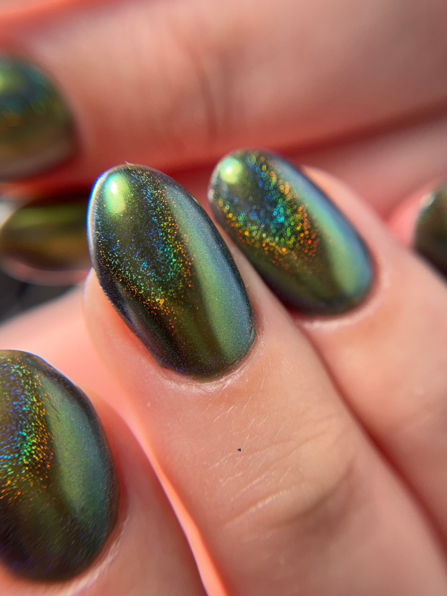 Close-up of a hand with metallic green nail color on a blurred background