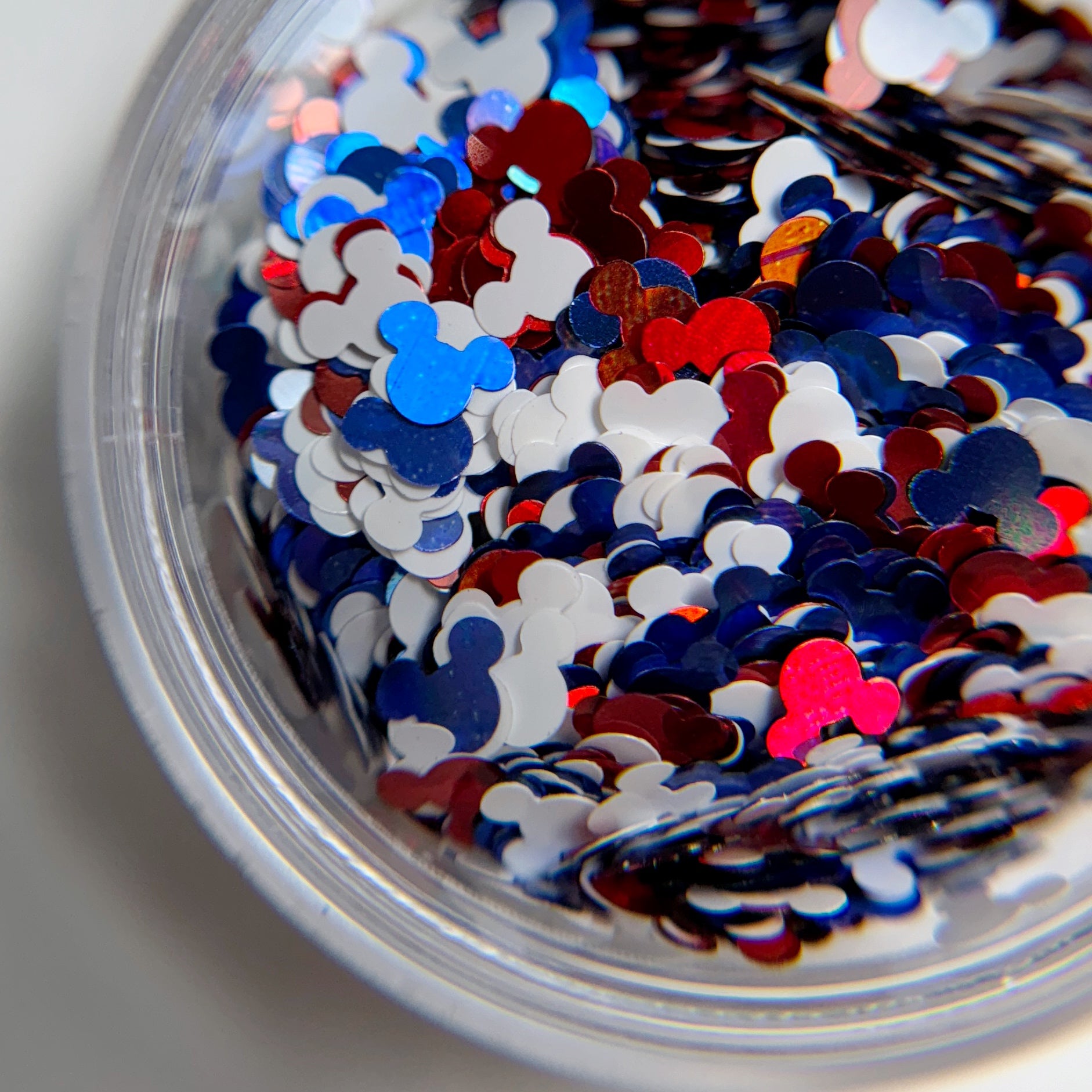 A close-up view of a bowl filled with mouse inspired glitter pieces, with a preponderance of red, blue, and white, representing a patriotic color scheme.