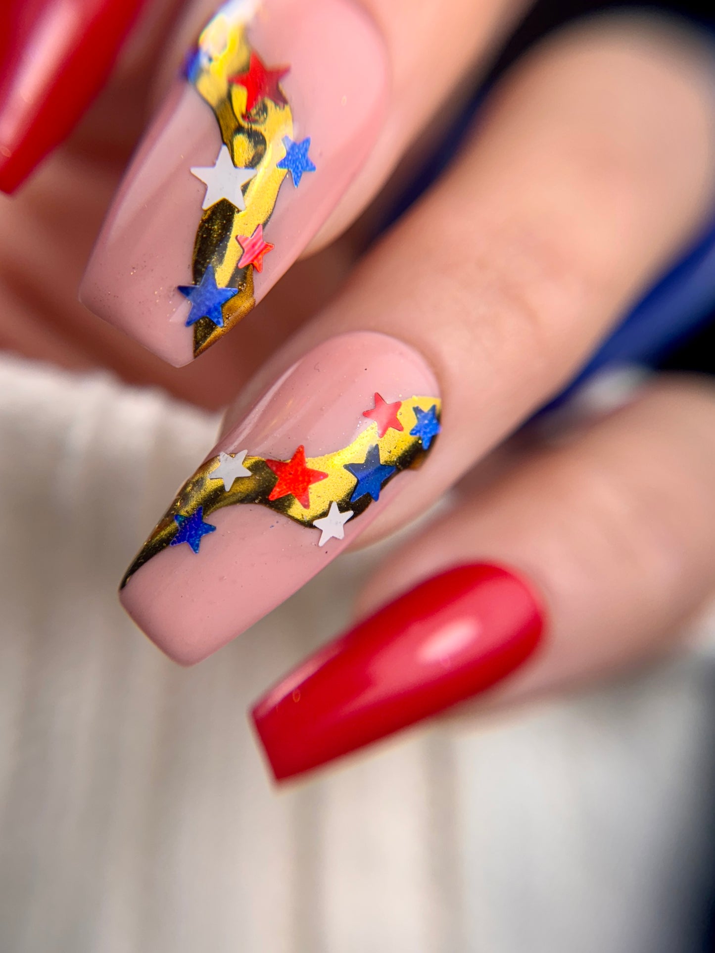 Nail art with colorful stars and red polish on a blurred background