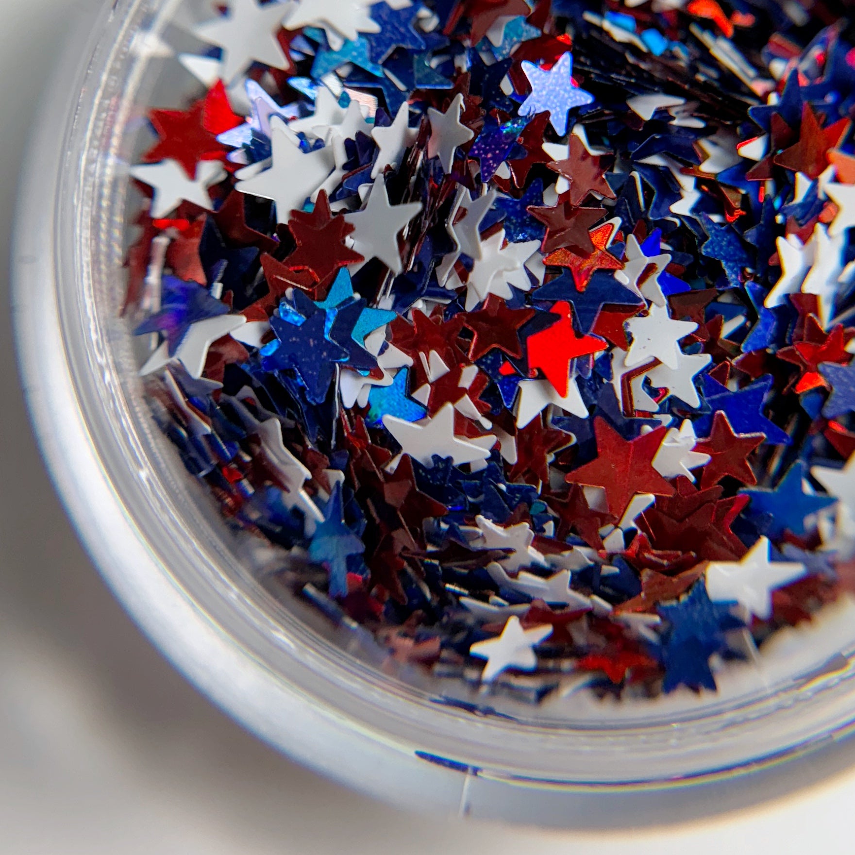 A close-up view of a container filled with red, blue, and silver star-shaped glitter pieces.