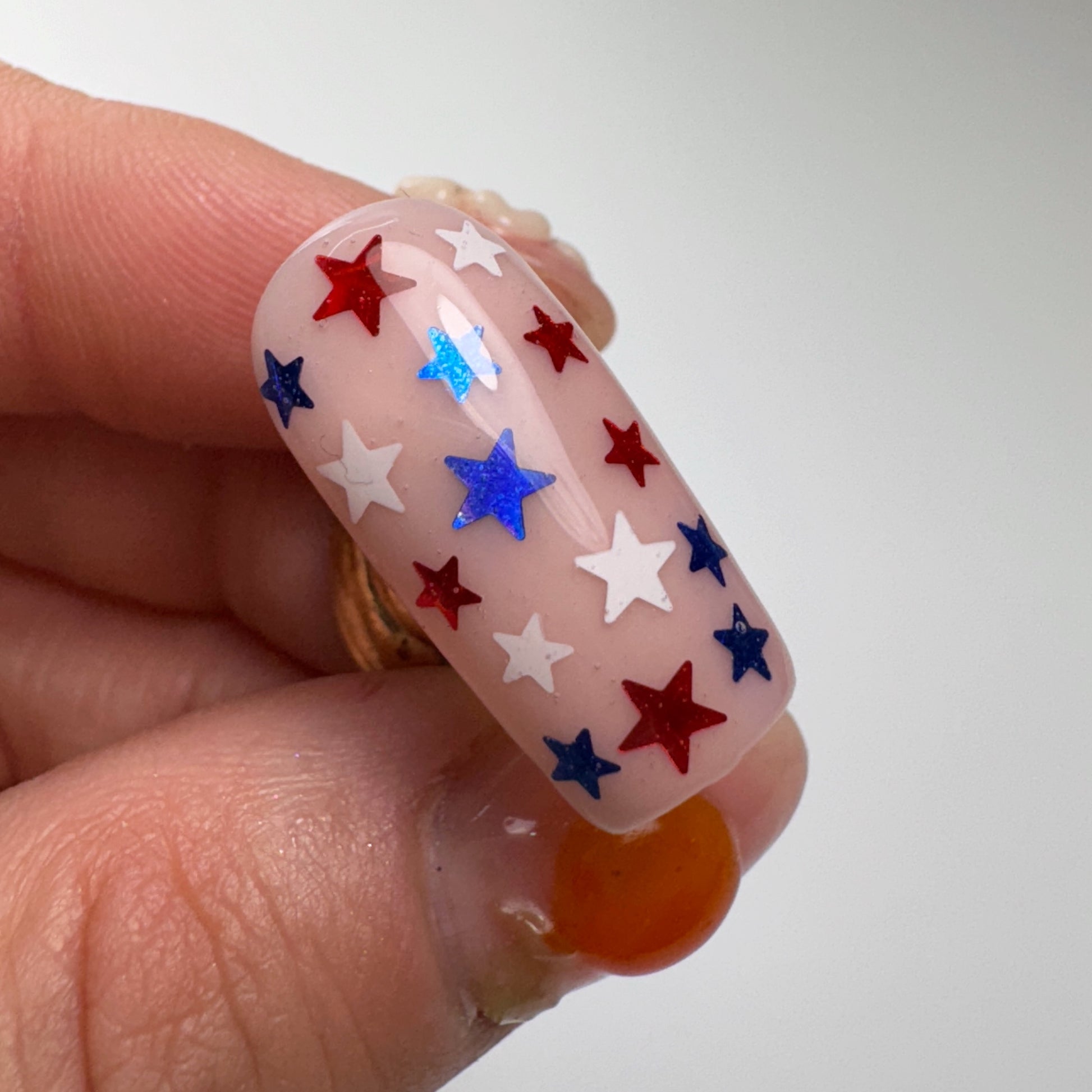 Hand holding decorated nail tip against light background.