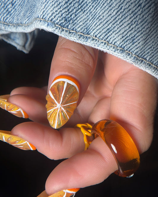Close-up of a hand with orange-themed nail art and a matching ring.
