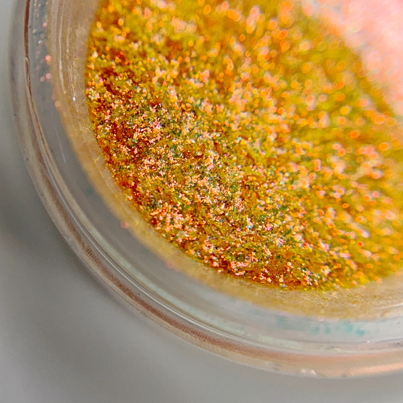Close-up view of a jar containing apricot-colored fine glitter on blurred background