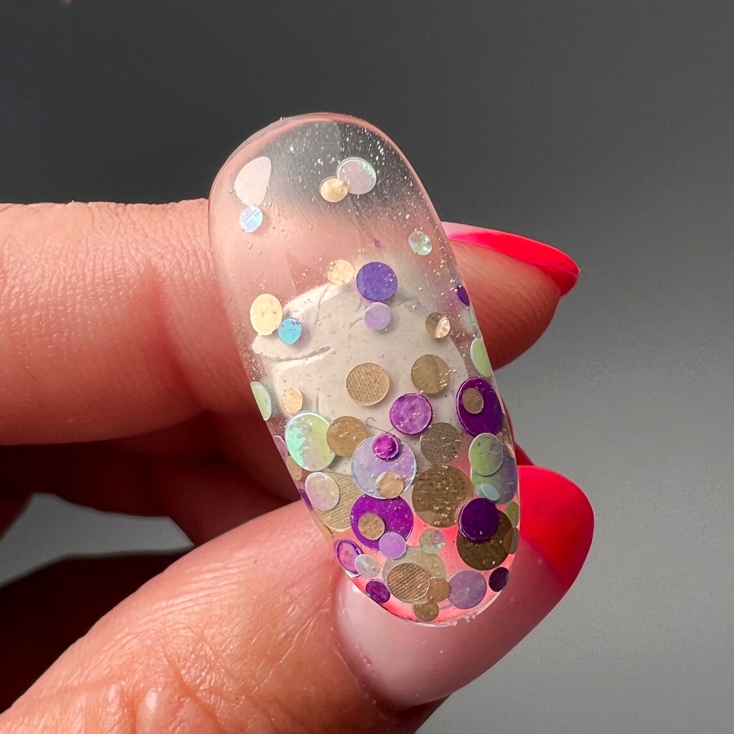 Hand holding a nail tip with art on gray background 