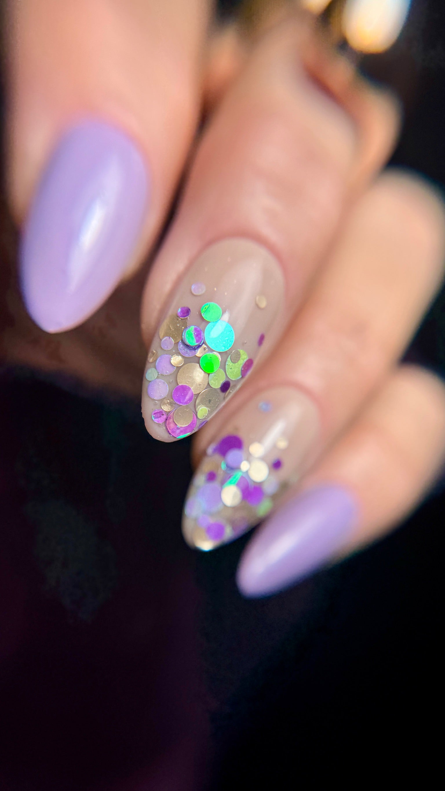 Nail art with purple polish and colorful glitter design on a dark background