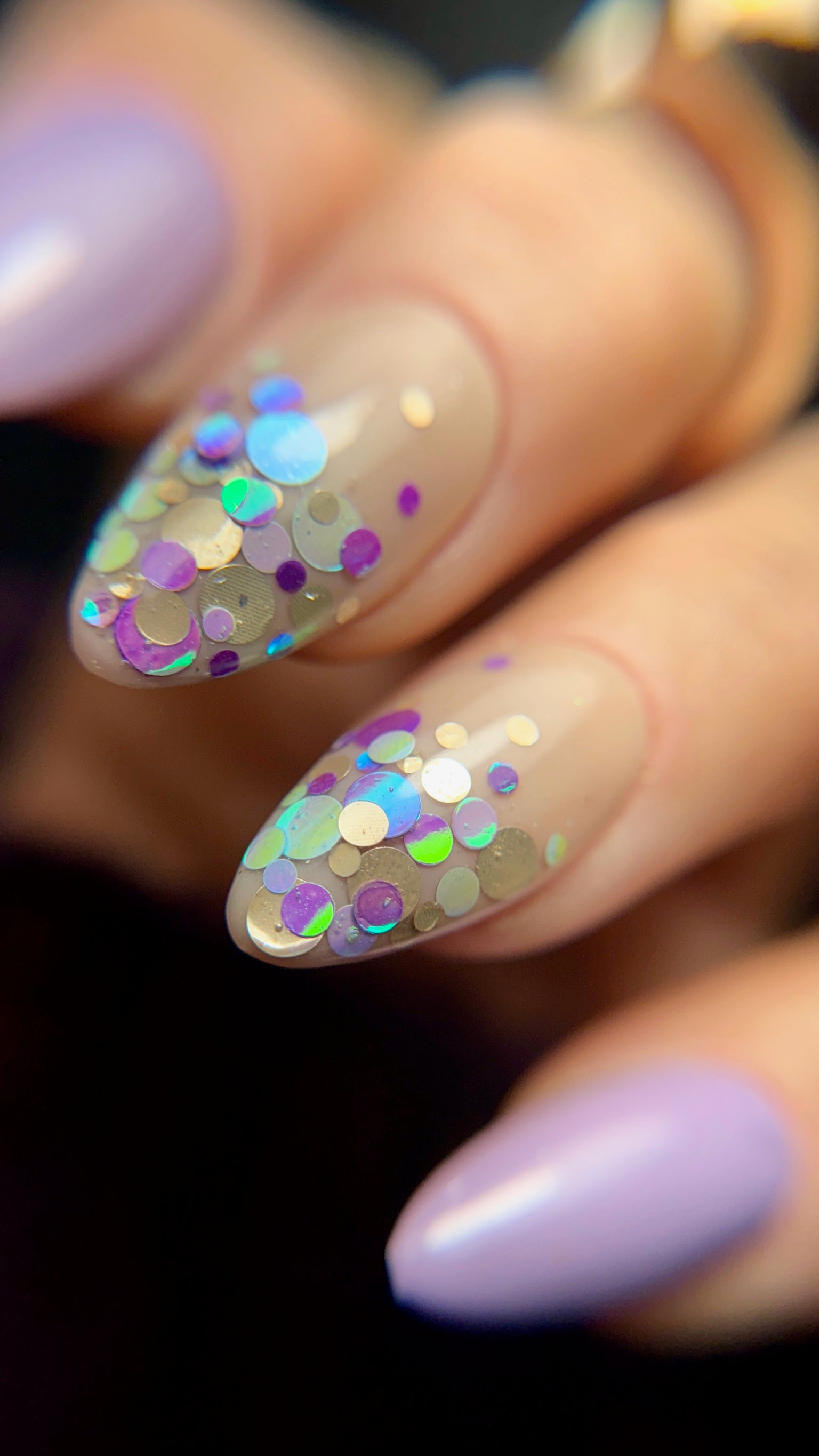 Nail art with purple polish and colorful glitter on a dark ackground