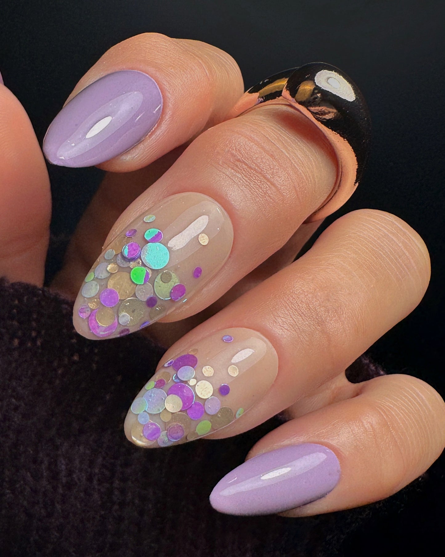Close-up of a hand with decorative nails featuring purple and gold and multicolored glitter.