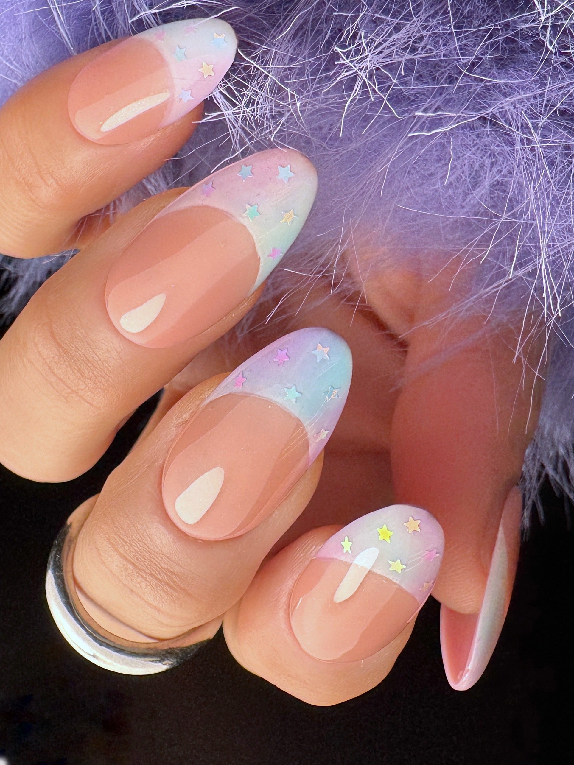 Nails with pastel designs held against a textured purple background