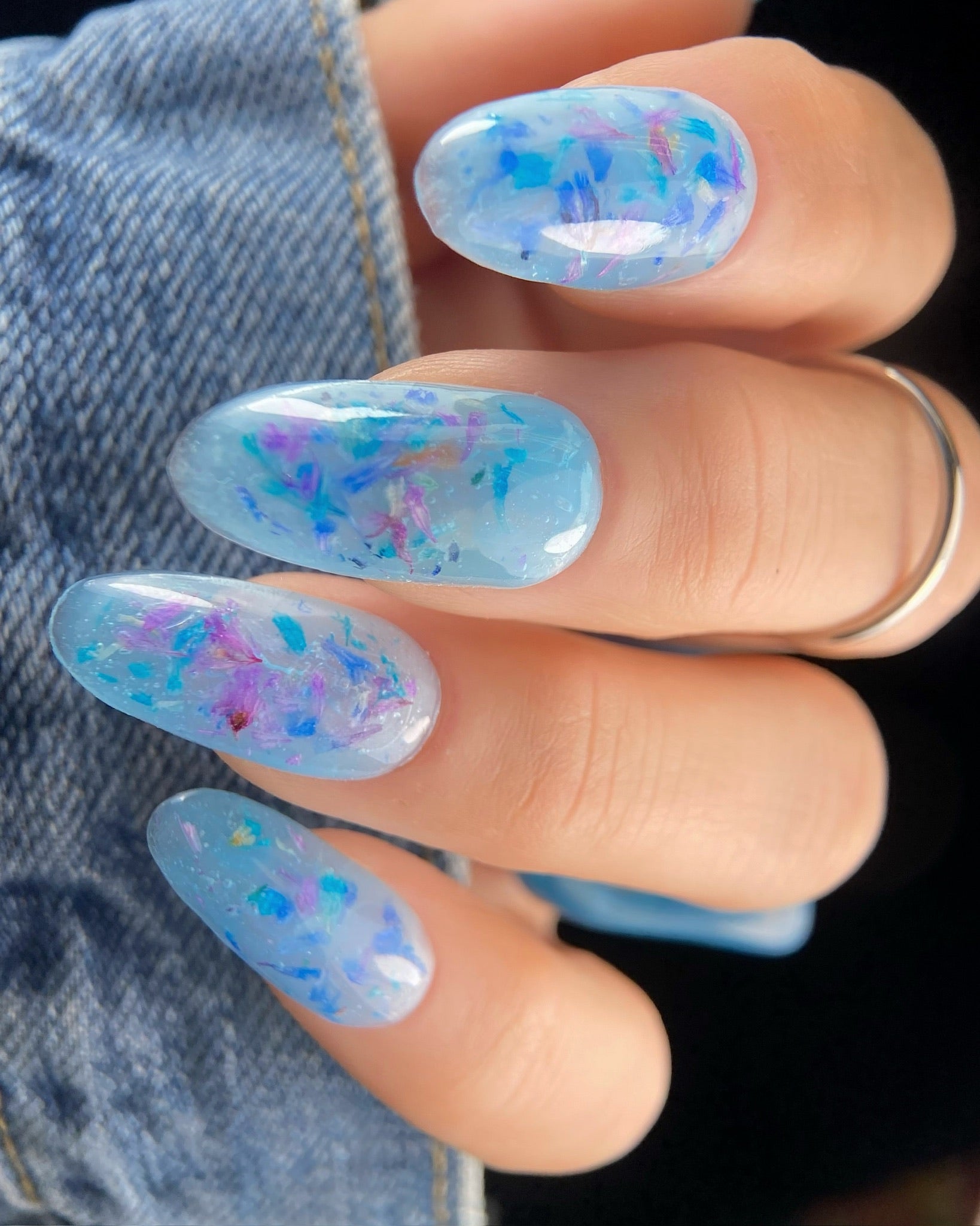 Hand in denim sleeve with with blue and purple floral design on nails.