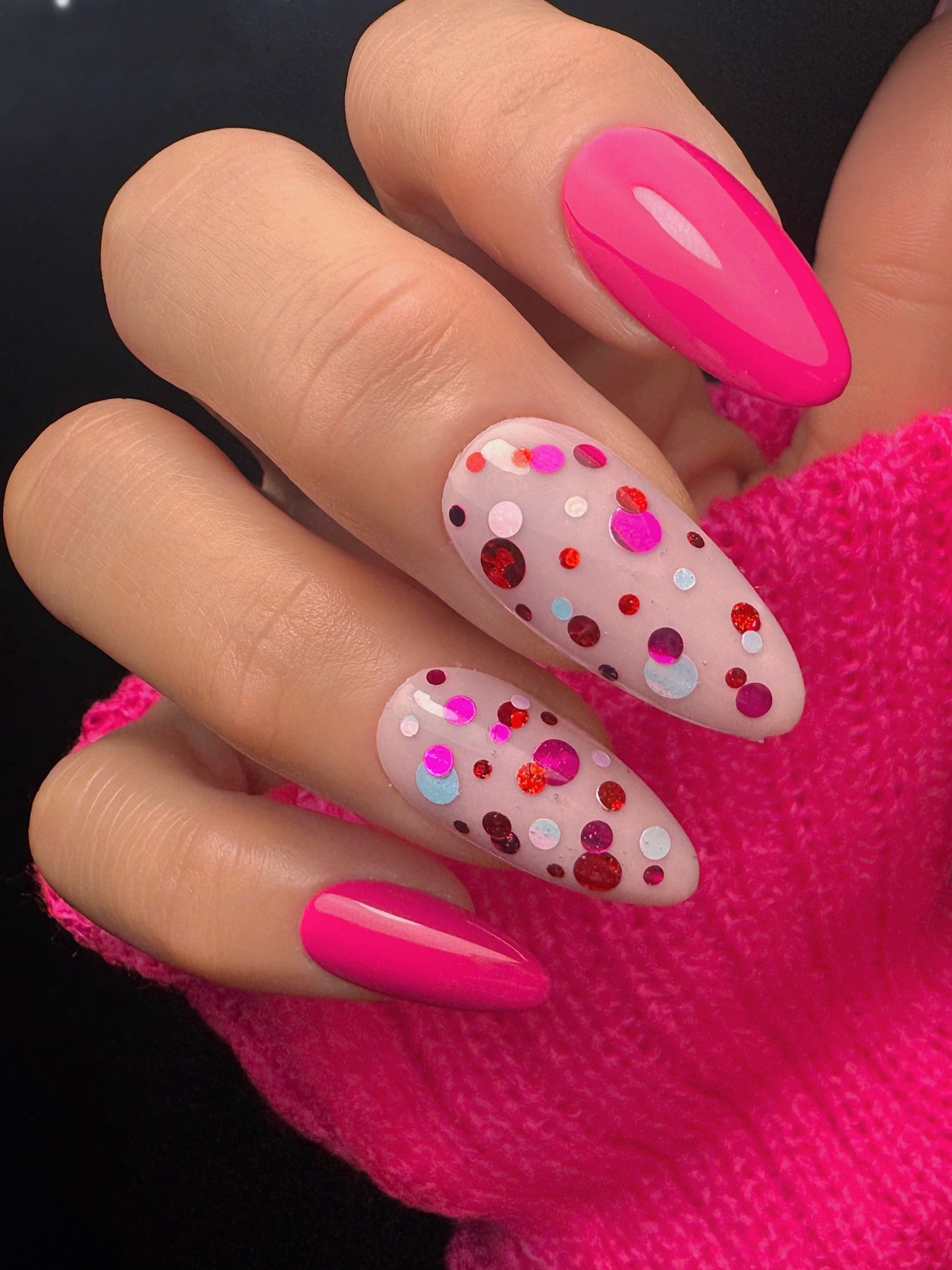 Close-up of a hand with pink and polka dot nail design against a dark background