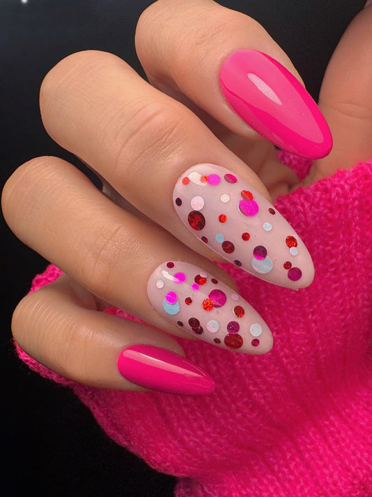 Close-up of a hand with pink and polka dot nail design against a dark background