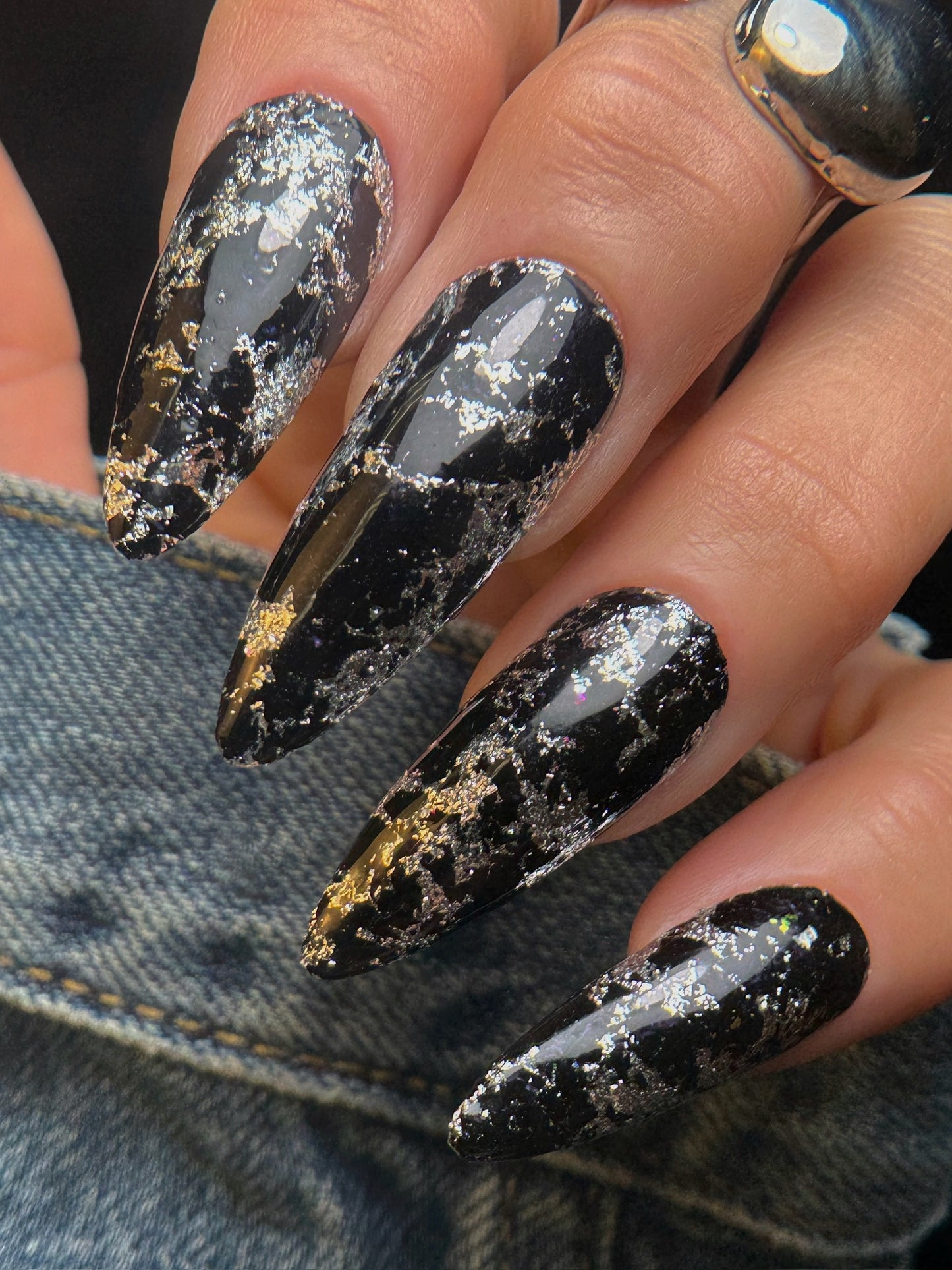 Black and silver glittery nails on a person's hand with denim background